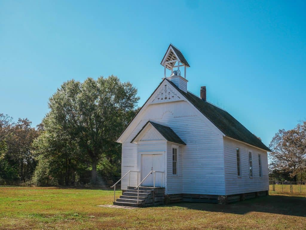 Small white church with steeple in a rural setting under a clear blue sky.