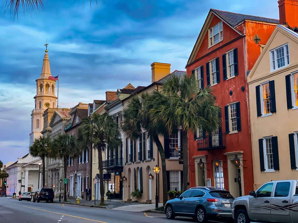 Historic Charleston colorful row houses with palm trees and church steeple in the background.