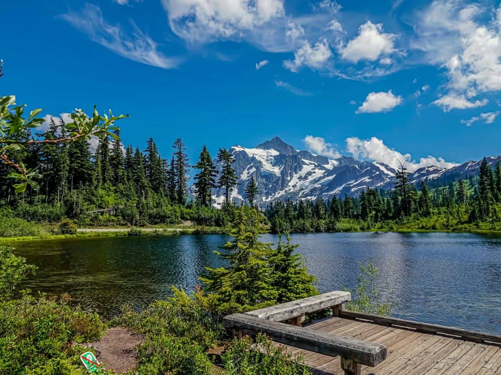 Mountain lake with pine trees and snow-capped peaks in the background.